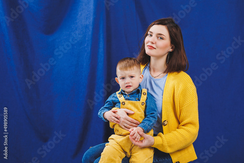 A young mother sits with a 3-year-old son in her arms, family relationships with a child. Children's education. Mom with son on a blue background