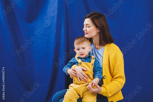 A young mother sits with a 3-year-old son in her arms, family relationships with a child. Children's education. Mom with son on a blue background