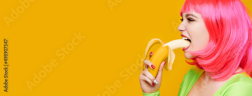 Sexy hipster woman in pink wig eat banana on bright yellow background