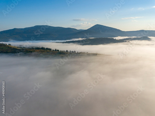 Flight over fog in Ukrainian Carpathians in summer. Mountains on the horizon. A thick layer of fog covers the mountains with a continuous carpet. Aerial drone view.