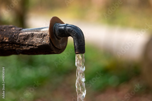 Drinking water fountain made out of wood and metal faucet. Flowing clear water, close up shot, shallow depth of field, forest scene, no people