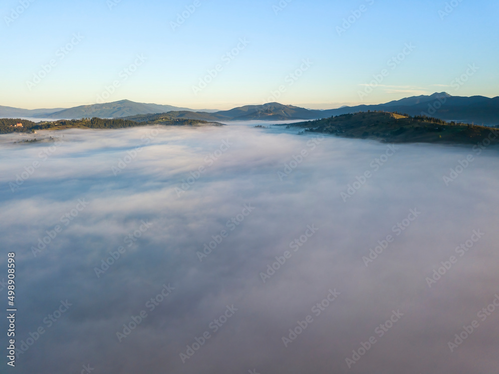 Flight over fog in Ukrainian Carpathians in summer. Mountains on the horizon. A thick layer of fog covers the mountains with a continuous carpet. Aerial drone view.