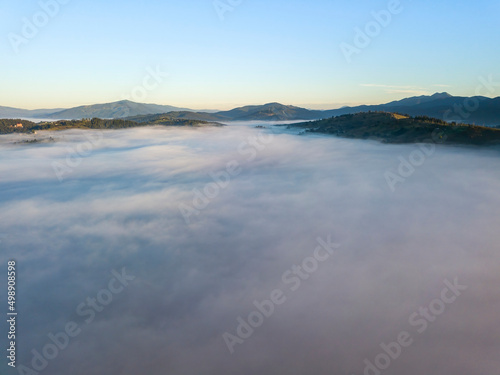 Flight over fog in Ukrainian Carpathians in summer. Mountains on the horizon. A thick layer of fog covers the mountains with a continuous carpet. Aerial drone view.