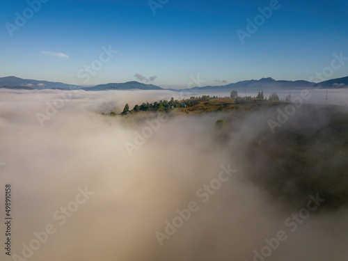 Flight over fog in Ukrainian Carpathians in summer. A thick layer of fog covers the mountains with a solid carpet. Mountains on the horizon. Aerial drone view.