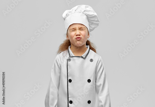cooking, culinary and profession concept - little girl in chef's toque and jacket over grey background