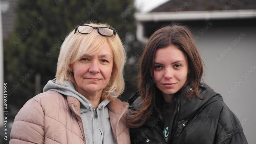 Mature mother and young daughter video portrait together outdoors on a windy cold day. Caucasian blond and brown haired women 