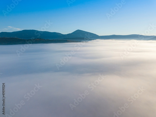 Flight over fog in Ukrainian Carpathians in summer. Mountains on the horizon. A thick layer of fog covers the mountains with a continuous carpet. Aerial drone view.