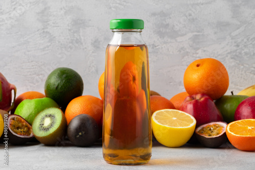 Various fruits and freshly squeezed fruits juice in bottle on gray background