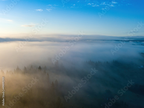 Sunny morning in the foggy Carpathians. A thin layer of fog covers the mountains. Aerial drone view.
