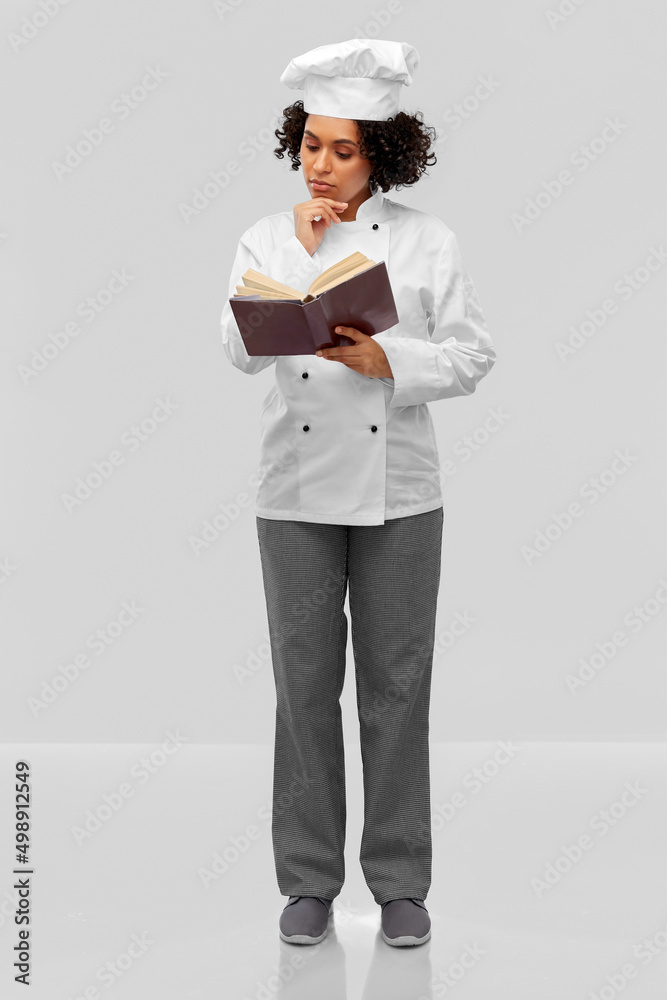 cooking, culinary and people concept - thinking female chef in white toque and jacket reading cook book over grey background cooking, culinary and people concept - thinking female chef in white toque and jacket reading cook book over grey background