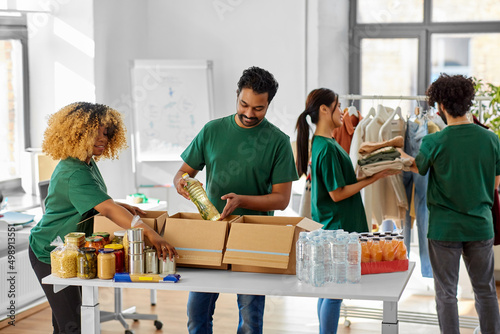 charity, donation and volunteering concept - international group of happy smiling volunteers packing food and clothes in boxes at distribution or refugee assistance center