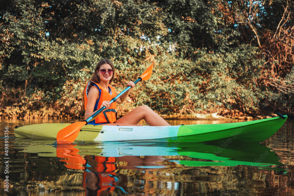 Kayaking on the river. A happy young tanned woman in a life jacket is floating in a kayak on the river. Concept of World Tourism Day