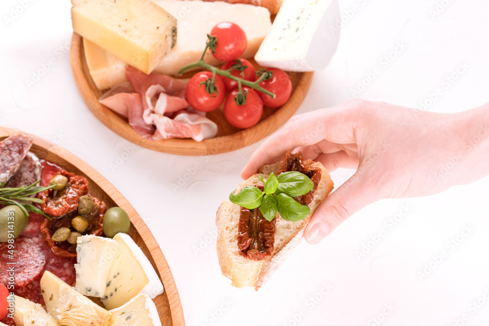 Top view on woman's hand holding bruschetta with sun dried tomatoes above table with traditional antipasti plates -selection of cheeses and sausages, proscuitto and olives. Selective focus
