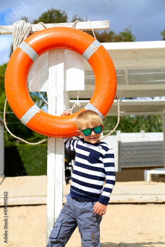 a boy in sunglasses standing by a lifebuoy on the beach