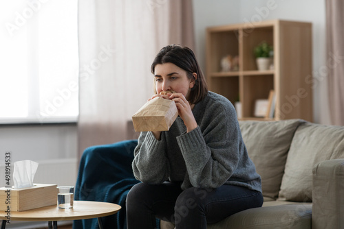 mental health and psychological problem concept - woman having panic attack breathing to bag at home