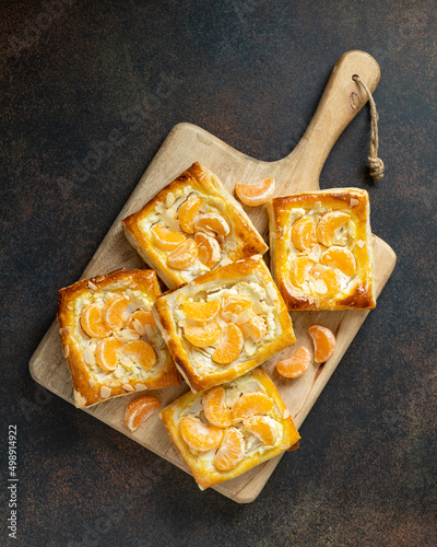 Mini puff pie with cheese cream, almonds, and tangerines in a plate on the kitchen table. Delicious layered square with citrus fruits, dorblue or ricotta, nuts on a culinary background top view photo