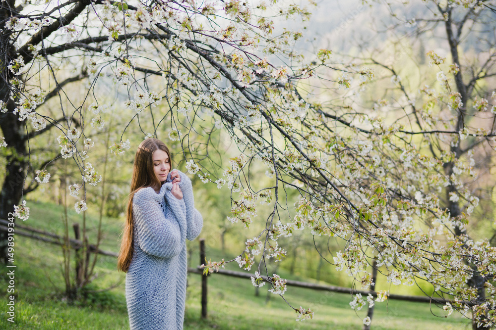 Young pretty emotional caucasian woman with long hair wearing natural makeup in romantic casual clothes walking among spring mountains near the beautiful fresh blooming tree in the countryside. Young pretty emotional caucasian woman with long hair wearing natural makeup in romantic casual clothes walking among spring mountains near the beautiful fresh blooming tree in the countryside.