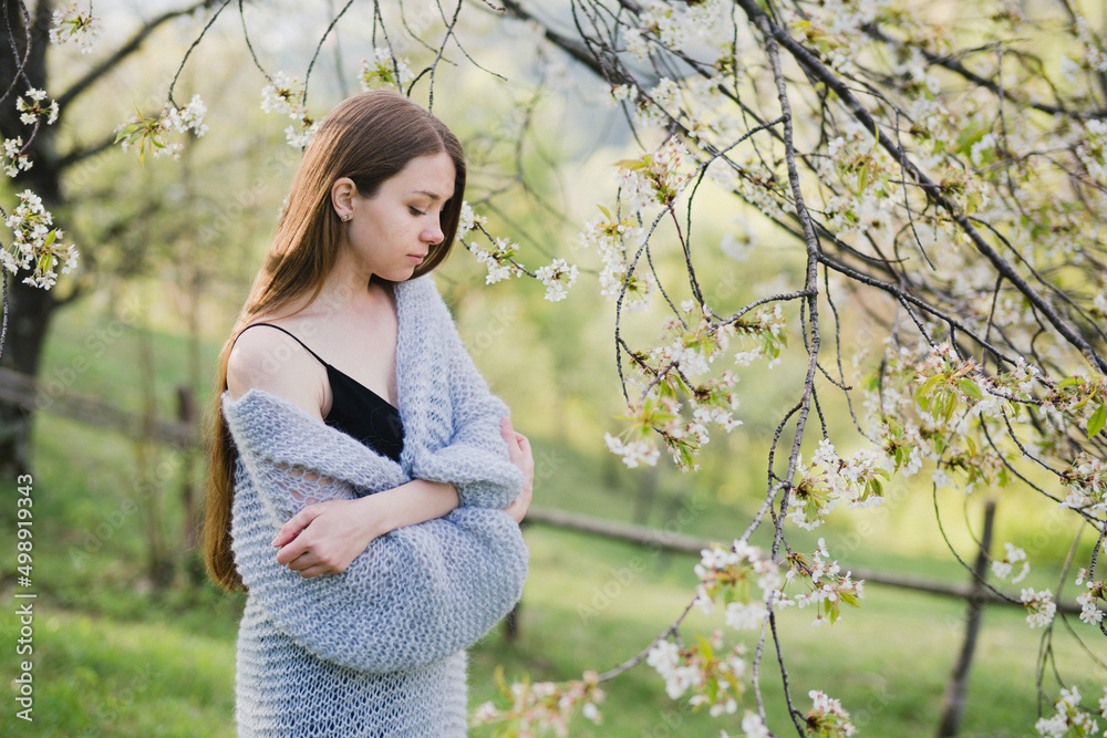 Young pretty emotional caucasian woman with long hair wearing natural makeup in romantic casual clothes walking among spring mountains near the beautiful fresh blooming tree in the countryside.
