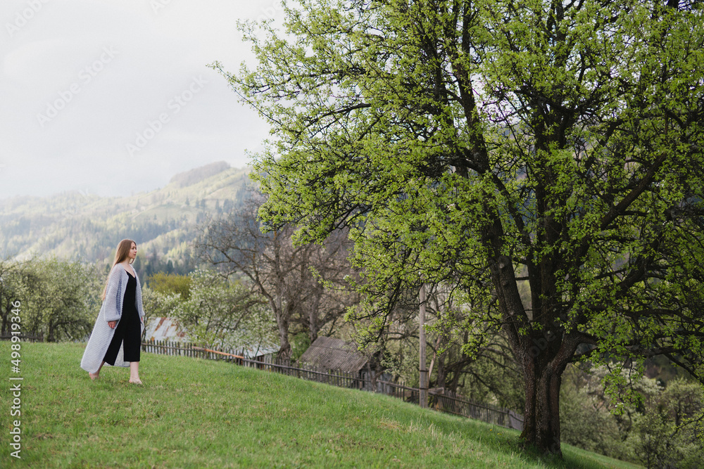 Young pretty emotional caucasian woman with long hair wearing natural makeup in romantic casual clothes walking among spring mountains near the beautiful fresh blooming tree in the countryside. Young pretty emotional caucasian woman with long hair wearing natural makeup in romantic casual clothes walking among spring mountains near the beautiful fresh blooming tree in the countryside.