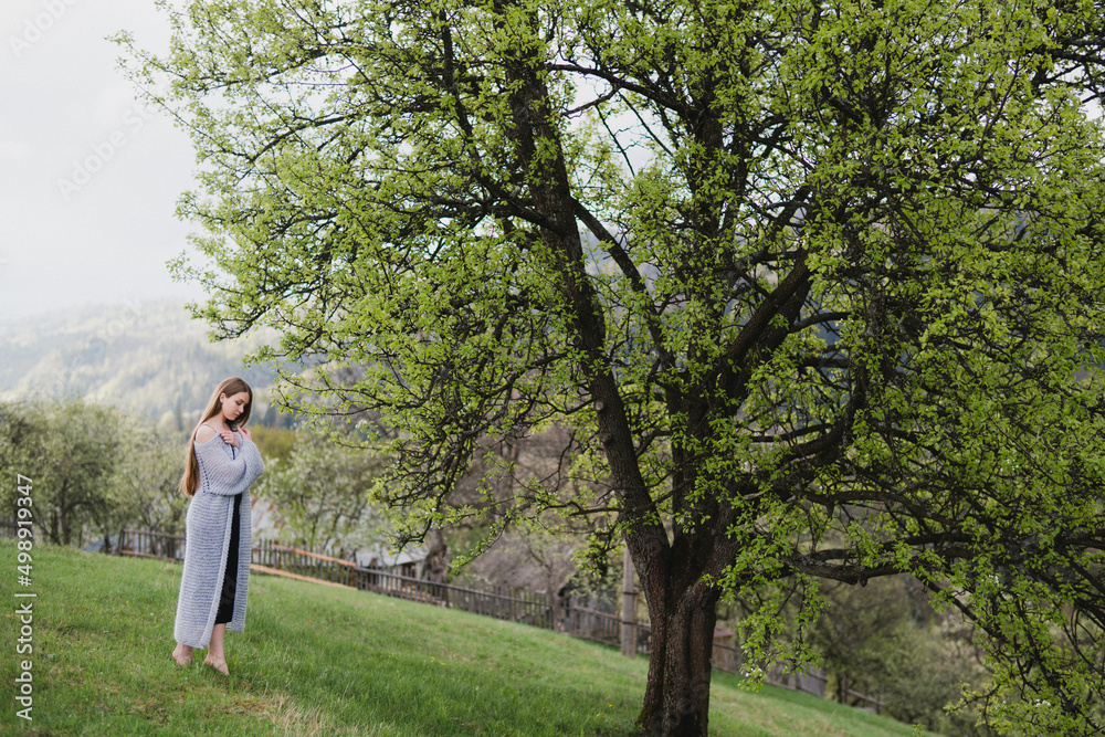 Young pretty emotional caucasian woman with long hair wearing natural makeup in romantic casual clothes walking among spring mountains near the beautiful fresh blooming tree in the countryside. Young pretty emotional caucasian woman with long hair wearing natural makeup in romantic casual clothes walking among spring mountains near the beautiful fresh blooming tree in the countryside.
