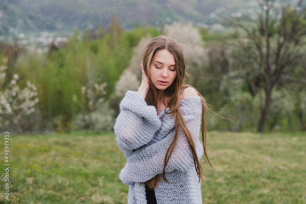 Obraz premium Young pretty emotional caucasian woman with long hair wearing natural makeup in romantic casual clothes walking among spring mountains near the beautiful fresh blooming tree in the countryside.