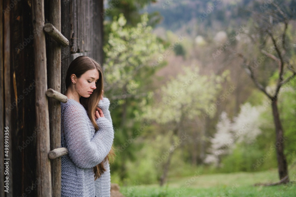 Young pretty emotional caucasian woman with long hair wearing natural makeup in romantic casual clothes walking among spring mountains near the beautiful fresh blooming tree in the countryside.