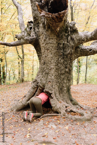 back of Woman trying hide in hole of old tree in forest