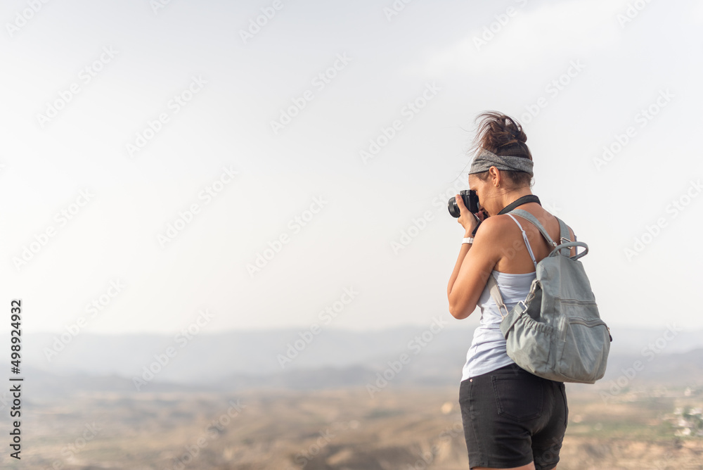 Anonymous woman with backpack taking photo in mountains