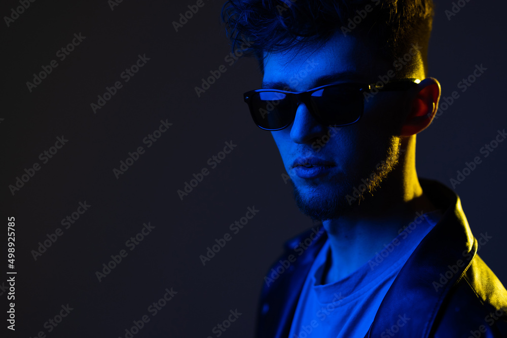Young man's portrait isolated on blue studio background in neon light. Beautiful male model in leather wear. Concept of human emotions, facial expression, sales, ad. Young man's portrait isolated on blue studio background in neon light. Beautiful male model in leather wear. Concept of human emotions, facial expression, sales, ad.