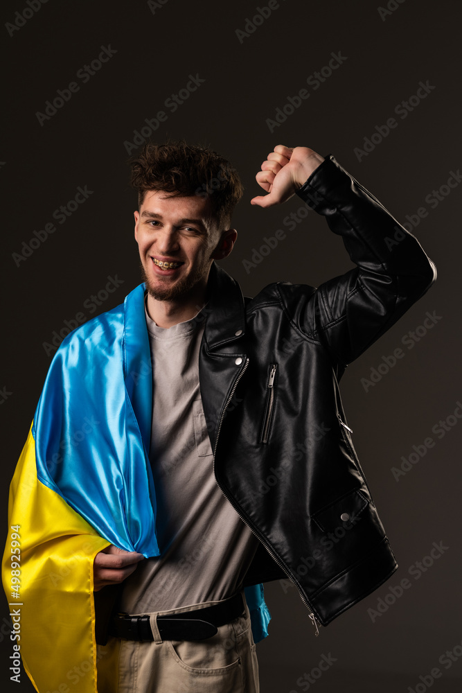Young man holding a flag of Ukraine smiling confident with crossed arms ion a black background. Young man holding a flag of Ukraine smiling confident with crossed arms ion a black background.