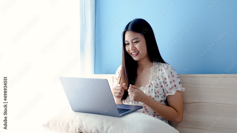 Beautiful Asian girl, wearing a floral shirt, is ordering online on a laptop computer, happily, holding a credit card in her hand, picking up to pay with a credit card,online shopping. Beautiful Asian girl, wearing a floral shirt, is ordering online on a laptop computer, happily, holding a credit card in her hand, picking up to pay with a credit card,online shopping.