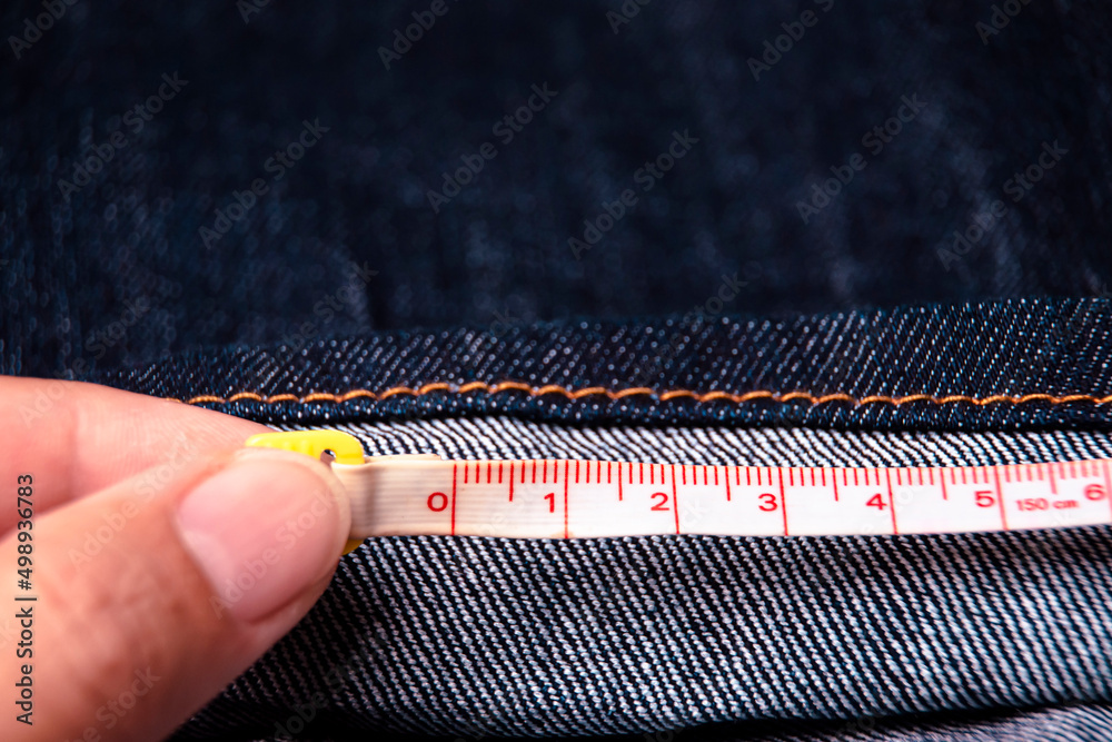 Hand of tailor measure the length of the jeans with a measuring tape - obrazy, fototapety, plakaty 