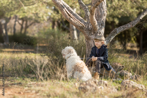a little boy in vintage clothes walks in nature with a white shaggy dog in spring.. © Olga