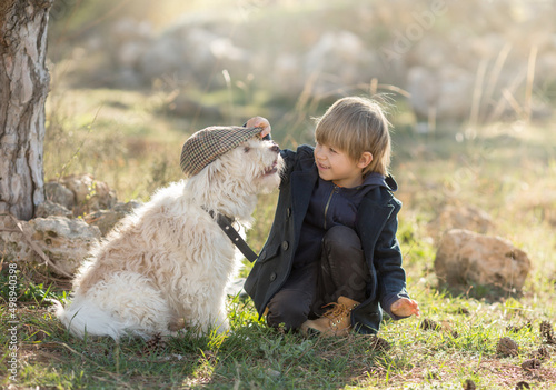a little boy in vintage clothes walks in nature with a white shaggy dog in spring..