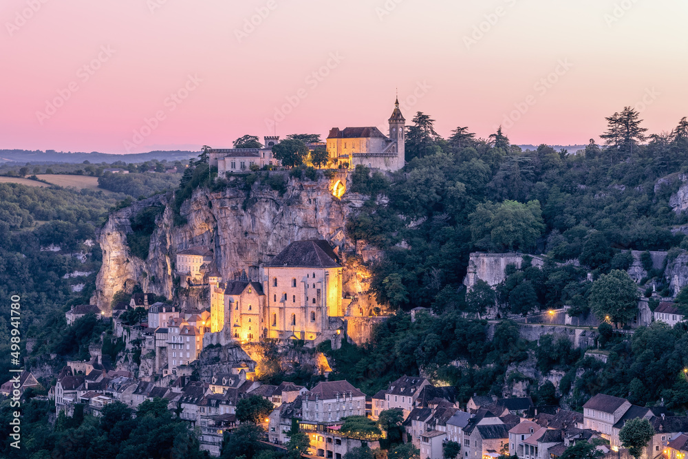 During summer twilight, first spotlights begin to illuminate most significant religious places of fabulous city of Rocamadour. Lot, Occitania, Southwestern France