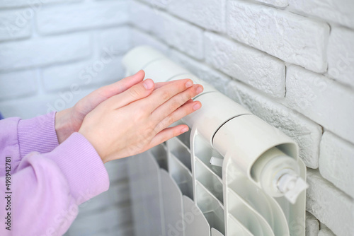 The child s hands warm their hands near the heating radiator. Saving gas in the heating season.