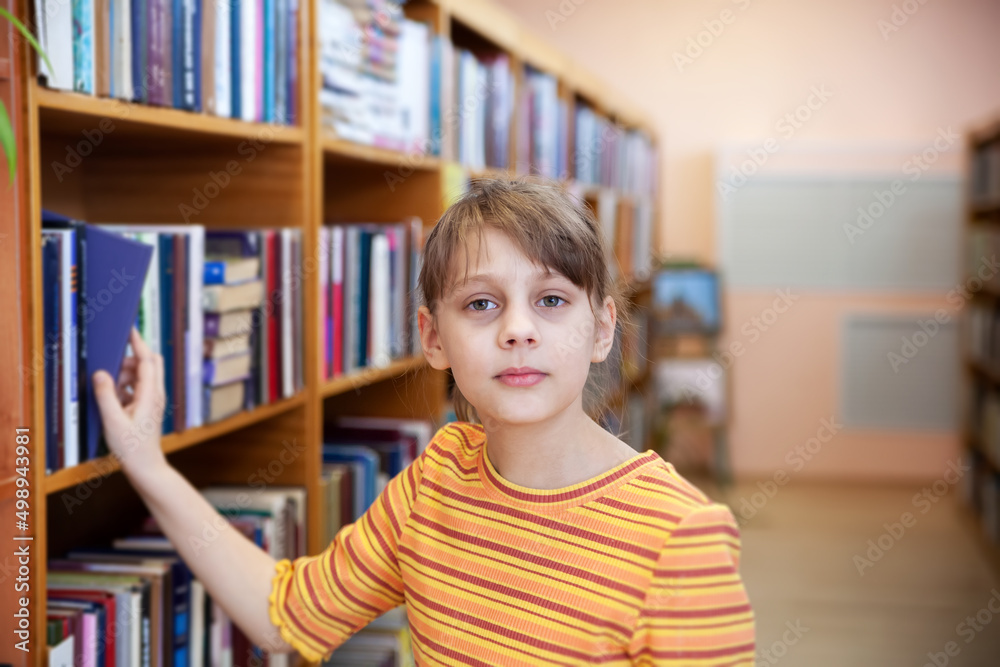Child near bookshelves and reading at school's library. Child near bookshelves and reading at school's library.