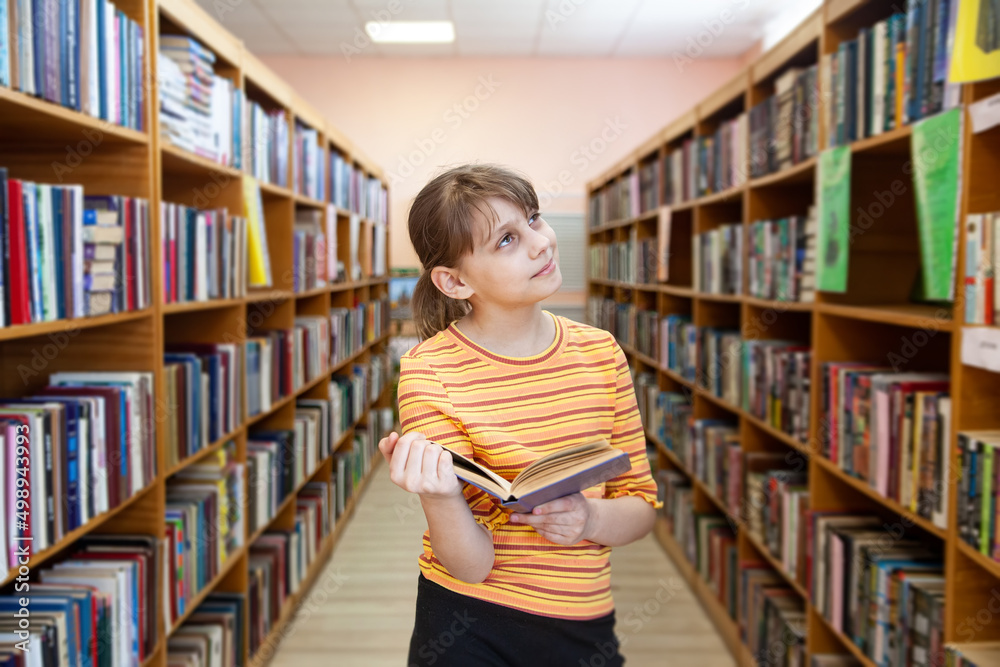 Child near bookshelves and reading at school's library. Child near bookshelves and reading at school's library.