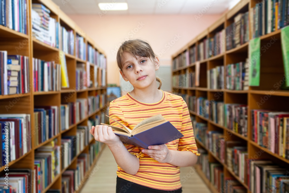 Child near bookshelves and reading at school's library. Child near bookshelves and reading at school's library.