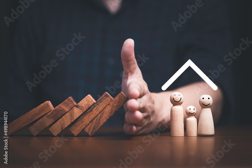 Businessman hand stop wooden block falling to protect family for assurance life and asset concept.