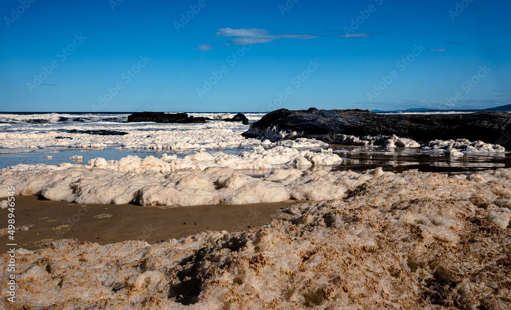 Landscape view of sea foam created during a massive storm approach the sbeach face with reflections in the sandy beach.