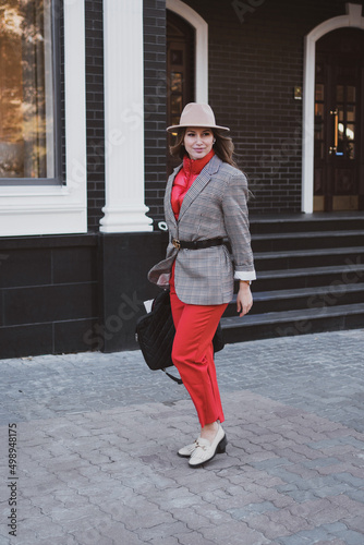 Stylish business woman in jacket and felt hat walks on the city street
