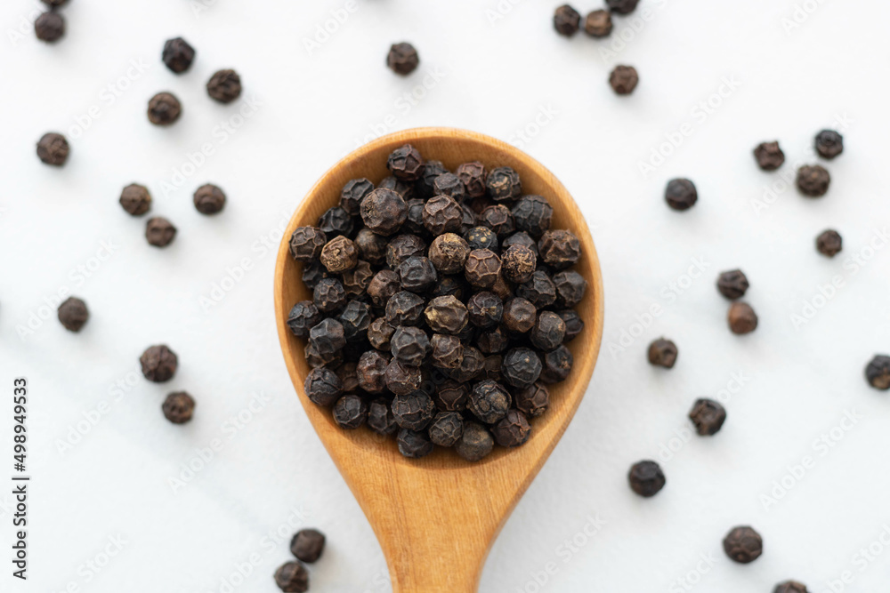 Black peppercorn with a wooden spoon on white background. Composition isolated over the white background. Black peppercorn with a wooden spoon on white background. Composition isolated over the white background.