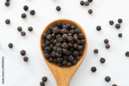 Black peppercorn with a wooden spoon on white background. Composition isolated over the white background.