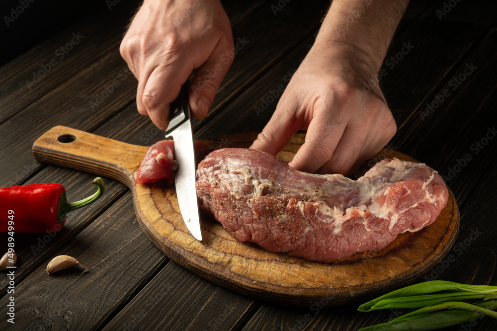 Close-up of a chef hands cutting raw veal meat on a cutting board before cooking. Peasant foods.