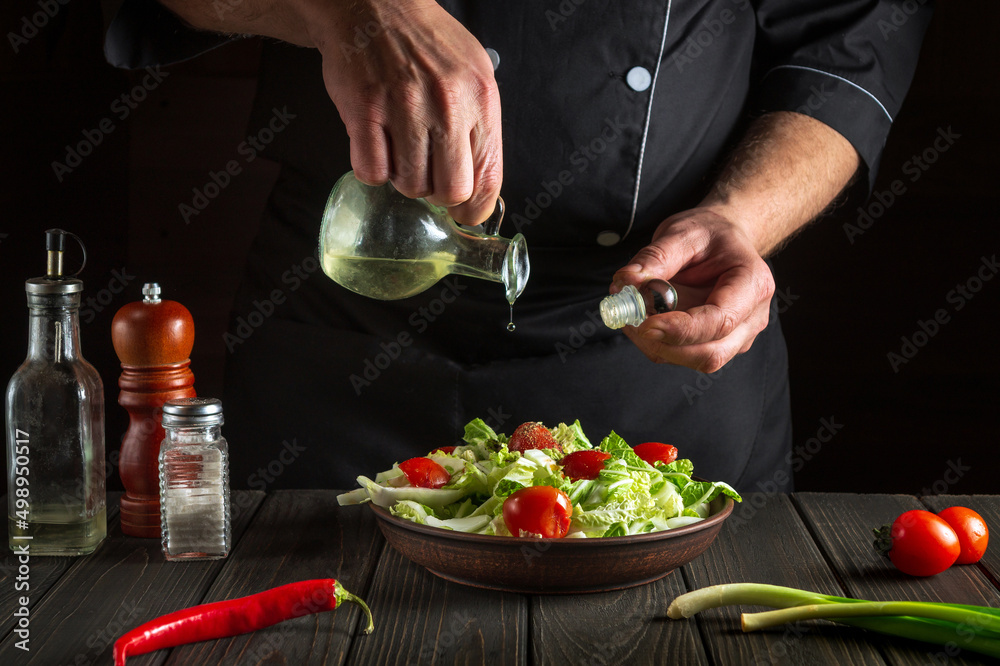Professional chef pours olive oil into a bowl of salad. Cooking tasty and healthy food with set of vitamins