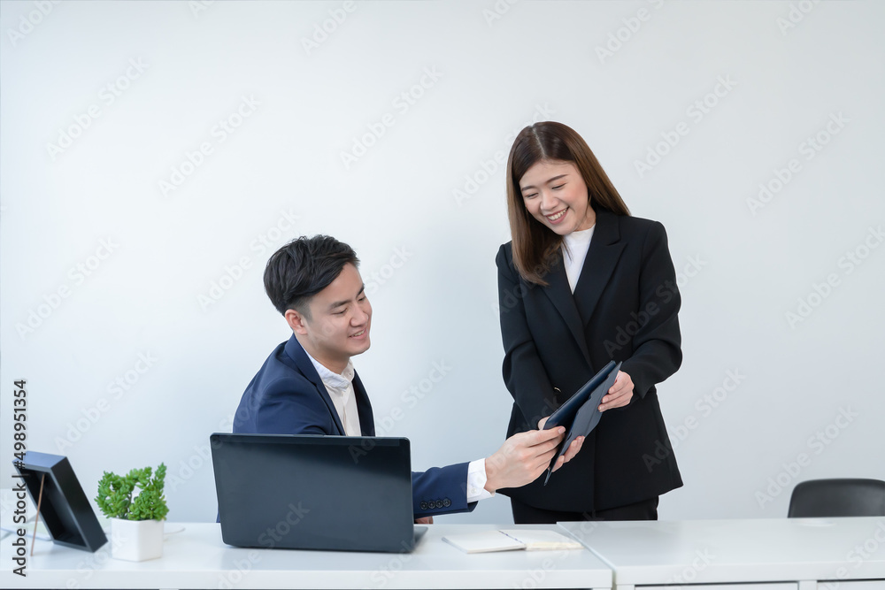 Asian secretary woman is holding and showing company performance report on tablet to her young handsome boss at office with a smiling face. Business people working together with smart online devices Asian secretary woman is holding and showing company performance report on tablet to her young handsome boss at office with a smiling face. Business people working together with smart online devices