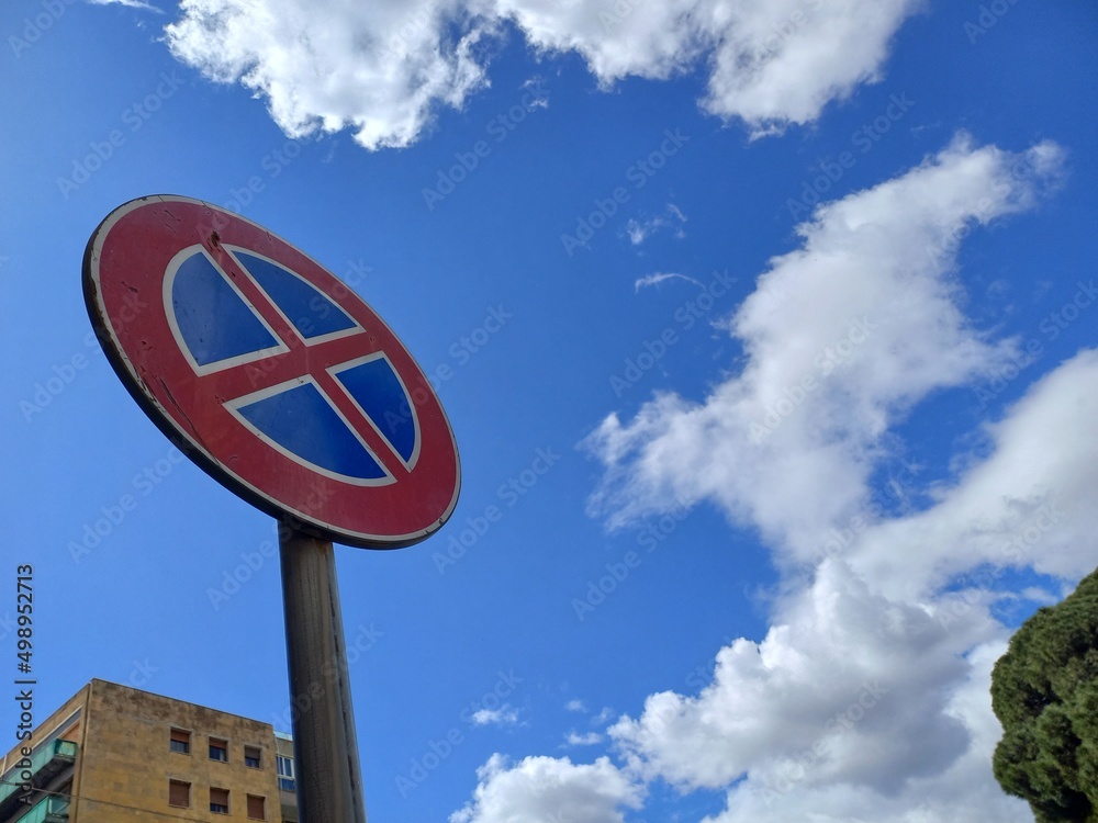 Segnale stradale rotondo rosso e blu con x che indica divieto di sosta e  fermata , con un cielo azzurro e un albero e un palazzo sullo sfondo Stock  Photo | Adobe Stock