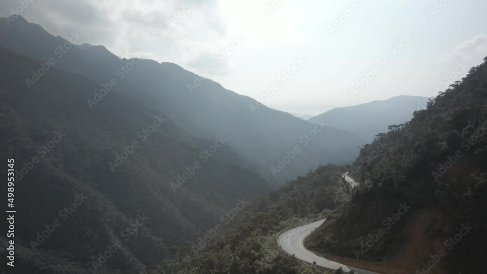 Ascending aerial shot of road in green MOuntains during foggy day and sunlight in background - Amazon Rainforest,Ecuador