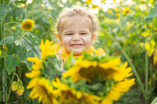 happy little kid girl playing in blooming sunflower field on sunny summer day